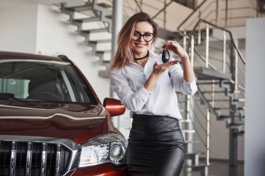 Yeni arabanı kullanırken iyi eğlenceler. Gözlüklü ve beyaz gömlekli kadın kırmızı otomobilin yanında duruyor..