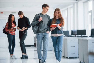 Kırmızı kapaklı kitaptan bilgi okuyor. Bir grup genç, mola zamanlarında ofiste yürüyorlar..