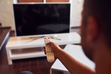İnsanın arka görünümü uzaktan kumandayı elinde tutuyor ve televizyonu açıyor.