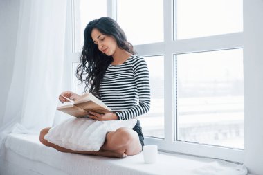 Sakin atmosfer. Pencerenin kenarında oturan kız kitap okuyor. Boş günün olması..