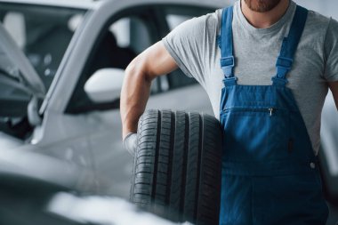 Tıraşsız adam. Tamirhanede lastik tutan bir tamirci. Kış ve yaz lastiklerinin değiştirilmesi.