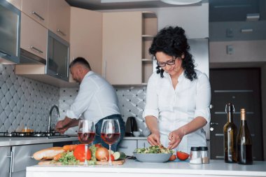 Sebze yıkıyorum. Beyaz gömlekli adam ve karısı mutfakta yemek hazırlıyorlar..