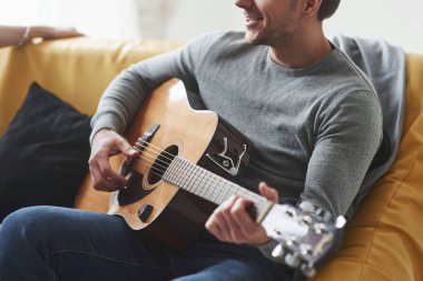 Sarı koltukta otururken akustik gitar çalan adam..