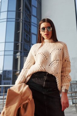 Paltoyu elinde tutuyor. Kalın elbiseli genç bir kız hafta sonları şehirde yürür..