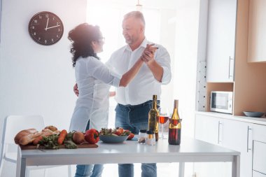 Güzel gün ışığında dans etmek. Yaşlı adam ve beyaz gömlekli karısı mutfakta romantik bir akşam yemeği yiyorlar..