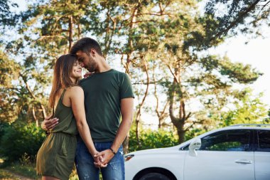 Beyaz otomobilin yanında duruyor. Genç ve güzel bir çift gündüz vakti ormanda iyi vakit geçirir..