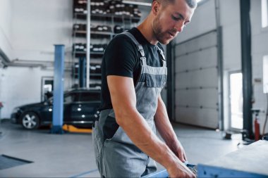 Doğru enstrümanları arıyorum. Erkek tamirci garajdaki bozuk otomobili tamir etmek için farklı araçlar kullanıyor.