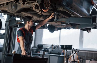 Araba yukarıda asılı duruyor. Atölyedeki üniformalı adam modern arabanın kırık parçalarını tamir ediyor..