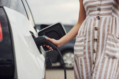 Elektrikli arabalardaki kadın gündüz şarj istasyonunda. Yepyeni bir araç..