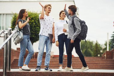 Çak bir beşlik. Gündüz vakti üniversitenin yakınlarında günlük giysiler içinde bir grup genç öğrenci.