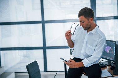 Masada oturuyor ve dinleniyor. Akıllı telefon ellerindeyken. Resmi giyinmiş genç işadamı birden fazla ekranla ofiste..