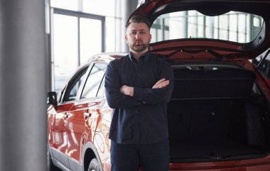 Kollarını kavuşturarak. Genç sakallı işadamının önü lüks kırmızı arabasının yanında duruyor..