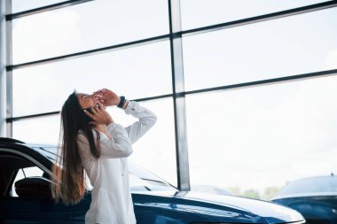 Telefonda sohbet ediyorduk. Beyaz elbiseli genç bir kadın mavi otomobilin önünde duruyor..