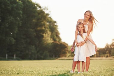 Kamera için poz vermek. Anne ve kızı dışarıda, tarlada yürüyüş yaparak hafta sonunun tadını çıkarıyorlar. Güzel doğa..