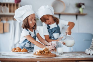 Kurabiyeler hazır. Beyaz şef üniformalı aile çocukları mutfakta yemek hazırlıyorlar..