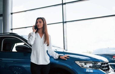 Telefonda sohbet ediyorduk. Beyaz elbiseli genç bir kadın mavi otomobilin önünde duruyor..