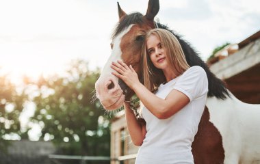 Gün batımında ayakta duruyor. Gündüz vakti atıyla çiftlikte mutlu bir kadın.
