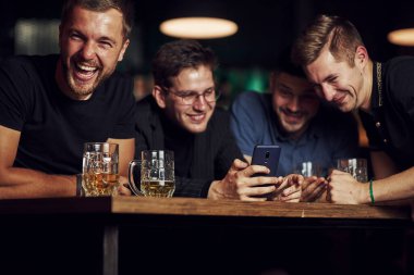 Akıllı telefondaki komik içerik. Barda elinde birayla dinlenen üç arkadaş. Sohbet ederken.