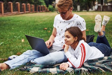 Genç çift sahada yeşil çimlerde dizüstü bilgisayarlarıyla oturuyor..