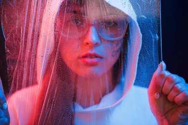 Üzerine su dökülen malzemelerin arkasında. Stüdyo karanlık stüdyoda neon ışıkla çekiliyor. Genç bir kızın portresi.