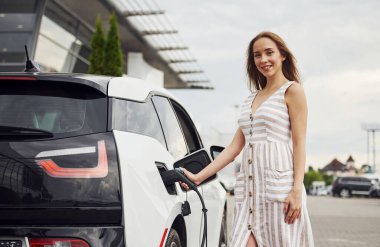 Elektrikli arabalardaki kadın gündüz şarj istasyonunda. Yepyeni bir araç..