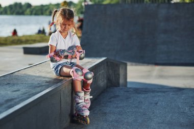 Açık havada patenli şirin küçük bir kız ekstrem sporlar için rampada oturuyor..