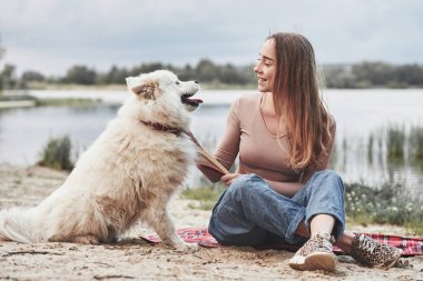 Birbirlerine bakıyorlar. Güzel beyaz köpeğiyle sarışın kız kumsalda harika vakit geçiriyor..
