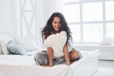 Ellerinin arasında yastıkla oturmak. Esmer, gündüz vakti yatak odasındaki beyaz kanepede dinleniyor..