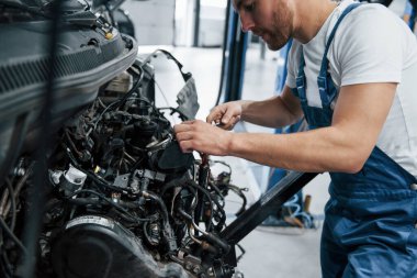 Her cıvata sıkı olmalı. Mavi üniformalı işçi otomobil salonunda çalışıyor..