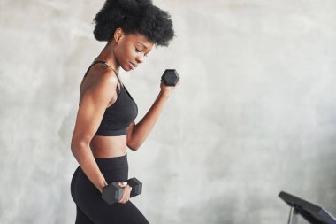 Pazılarla uğraşıyorum. Elinde dambıllarla gri arka planda duran genç bir kadının stüdyo çekimi..