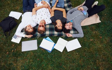 İyi dinleniyorum. Gündüz vakti yeşil çimlerde günlük giysiler içinde bir grup genç öğrenci..
