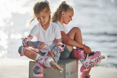 Arka planda göl kenarında patenli iki küçük kız..