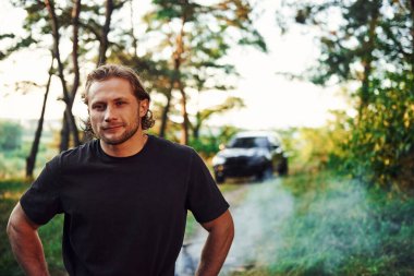 Ormanda durup doğaya bakan insanın portresi. Otomobil arkada park edilmiş..