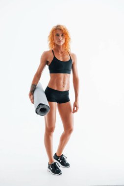 Gri renkli paspası elinde tutuyor. Kızıl saçlı kadın vücut geliştirici beyaz arka planda stüdyoda..
