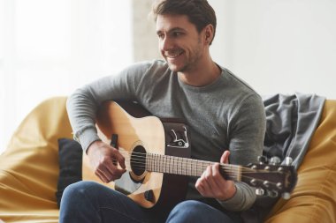 Hobbie ile iyi vakit geçiriyorum. Sarı koltukta otururken akustik gitar çalan adam..