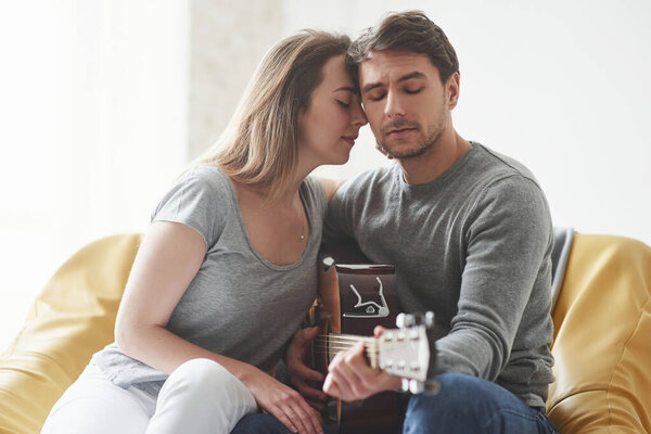 Concentrated at playing on acoustic guitar for the girlfriend in the living room of new house.