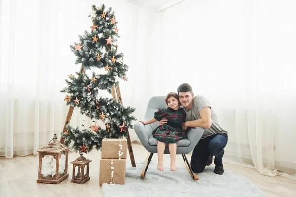 一起在房间里 圣诞节和节假日怀孕 可爱的小女孩和她的父亲坐在靠近梯子的椅子上 梯子上装饰着星星和地板上的礼品盒 — 图库照片