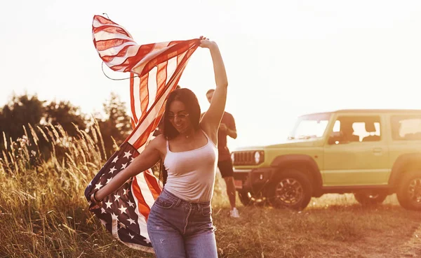 女孩向前跑 朋友们周末过得很愉快 在他们的绿色轿车旁边挂着美国国旗 — 图库照片