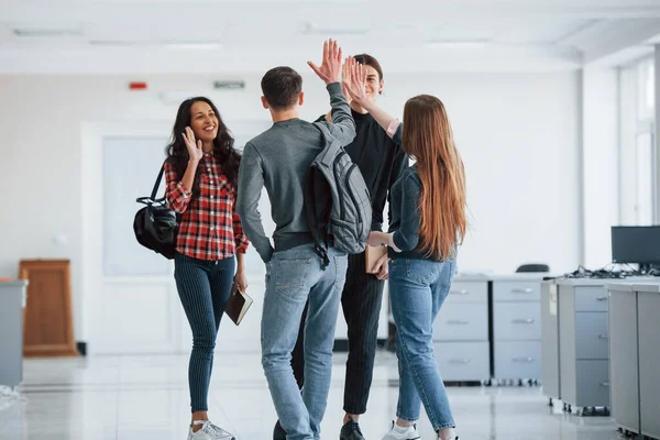 Giving high five. Group of young people walking in the office at their break time.
