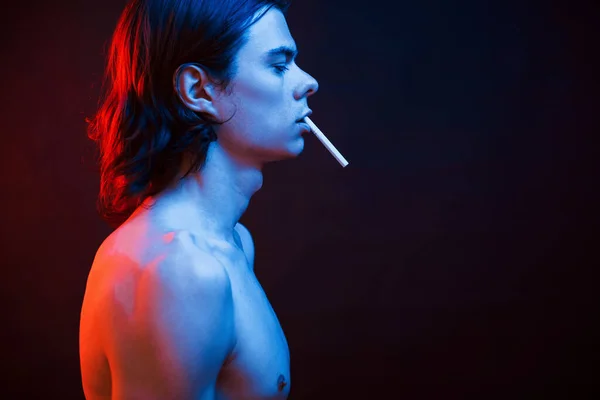 タバコを吸ってる スタジオはネオンで暗いスタジオで撮影しました 真剣な男の肖像 — ストック写真