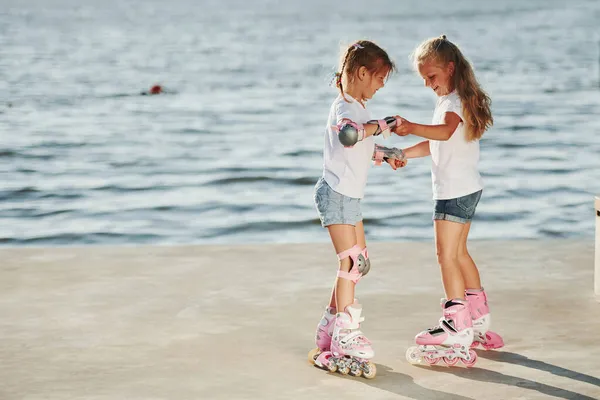 湖の近くの昼間にローラースケートに乗る方法を学ぶ2人の子供 — ストック写真