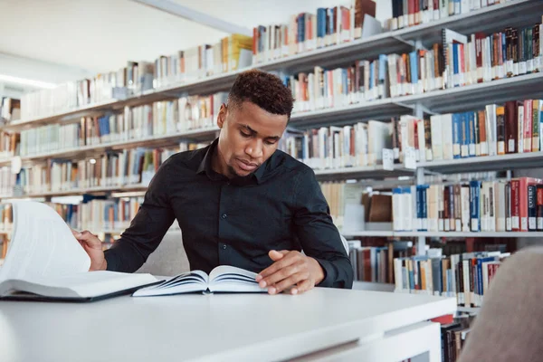 スタイリッシュな黒のシャツで アフリカ系アメリカ人の男性が図書館に座って本の情報を探しています — ストック写真