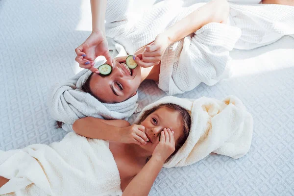 Young Positive Mother Daughter Towel Head Lying Bed Together Cucumber — Stock Photo, Image