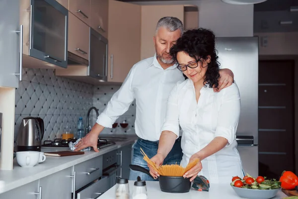 それが俺の秘密のレシピだ 台所で野菜を使った料理を作る白いシャツを着た男と妻 — ストック写真