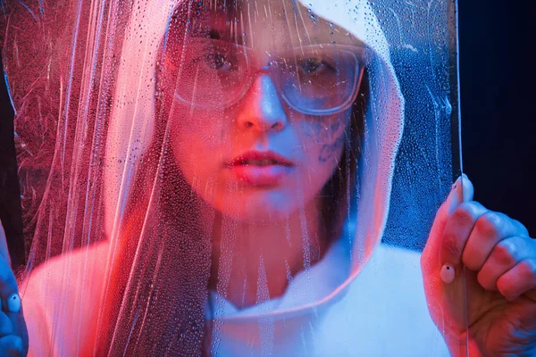 Üzerine su dökülen malzemelerin arkasında. Stüdyo karanlık stüdyoda neon ışıkla çekiliyor. Genç bir kızın portresi.