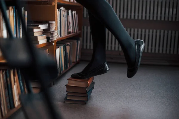 本の上に立って棚の上に到達しようとしています 女子学生は図書館にいる 教育の概念 — ストック写真
