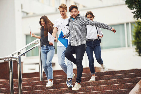 Walking on the stairs. Group of young students in casual clothes near university at daytime.
