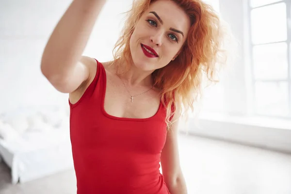 陽気な気分だ 魅力的な女性で赤いドレスと巻き毛でザ スペースルーム近くの窓 — ストック写真