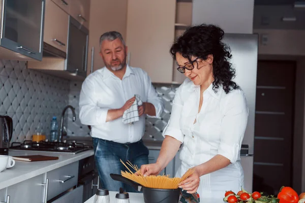 夕食がある 台所で野菜を使った料理を作る白いシャツを着た男と妻 — ストック写真