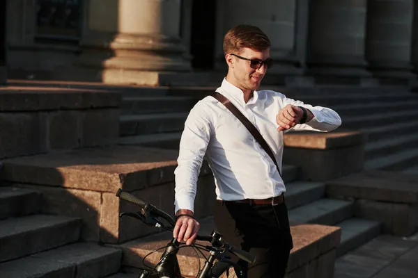時計の時刻を確認しろ 黒い自転車の正式な服を着たビジネスマンが街にいます — ストック写真